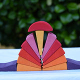 Pieces from the Glückskäfer wooden stacking sunray arch in yellow purple placed on a table. 