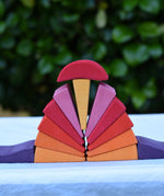 Pieces from the Glückskäfer wooden stacking sunray arch in yellow purple placed on a table. 