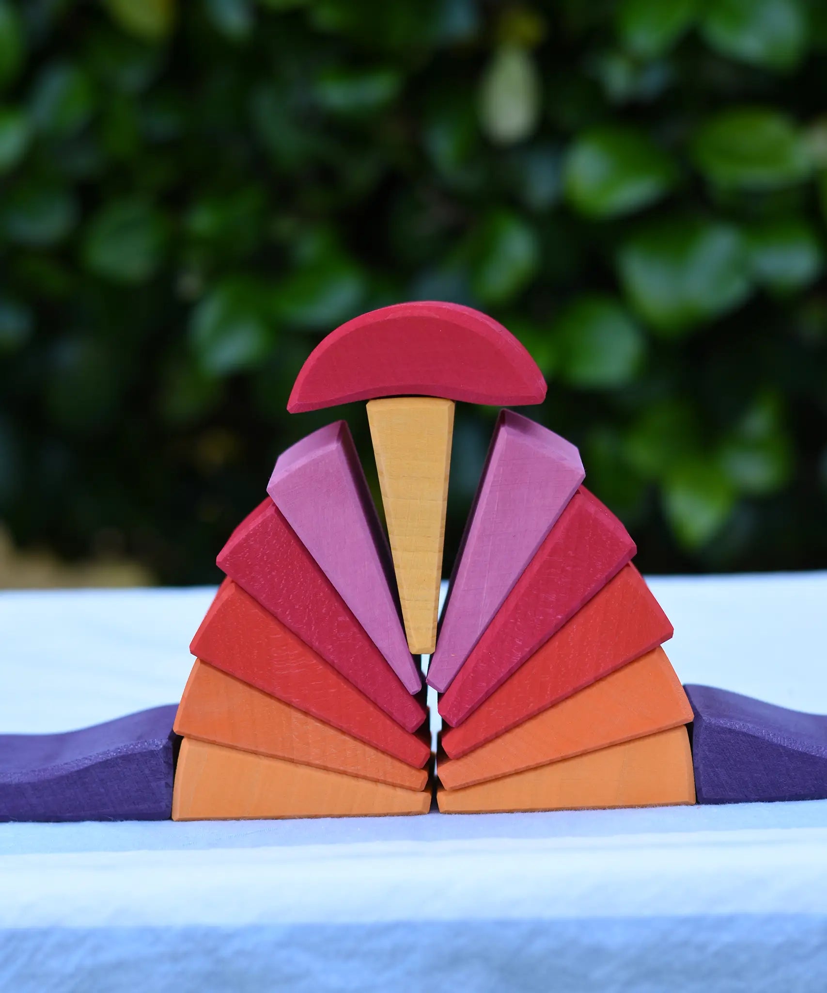 Pieces from the Glückskäfer wooden stacking sunray arch in yellow purple placed on a table. 