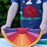 A child holding the Glückskäfer wooden stacking sunray arch in yellow purple placed on a table outdoors. 