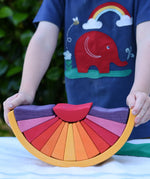 A child holding the Glückskäfer wooden stacking sunray arch in yellow purple placed on a table outdoors. 