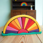 A Gluckskafer Yellow Sunray Arch pictured on a wooden surface. A dark wood miniature dresser can be seen in the background with a mini Grimm's rainbow placed on one of the shaves