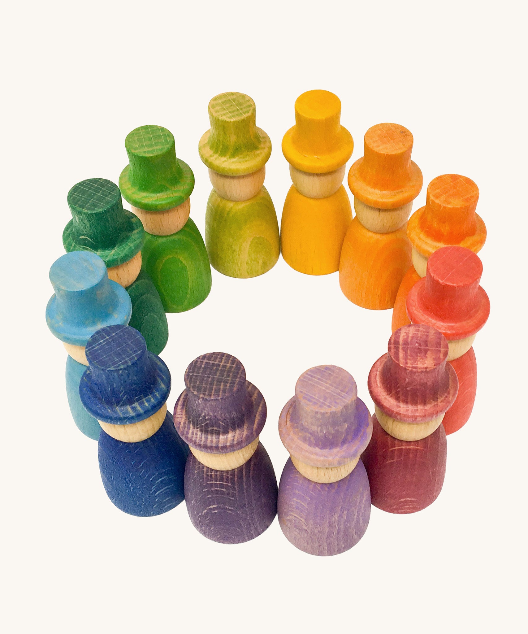 Grapat 12 Magos wooden peg dolls with top hats in a rainbow of 12 colours placed in a circle. These wooden toys are part of a wide range of open ended toys available at Babipur.  