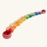 The Grapat 12 Rainbow Wooden Sorting Bowls all lined up and filled with loose parts and natural bits in matching colours. These Grapat bowls are part of a big range of open ended wooden toys available at Babipur.  