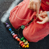 Close up of a child's hand threading colourful wooden beads onto a string from one of the gifts included in the Grapat 2026 advent calendar available at Babipur.