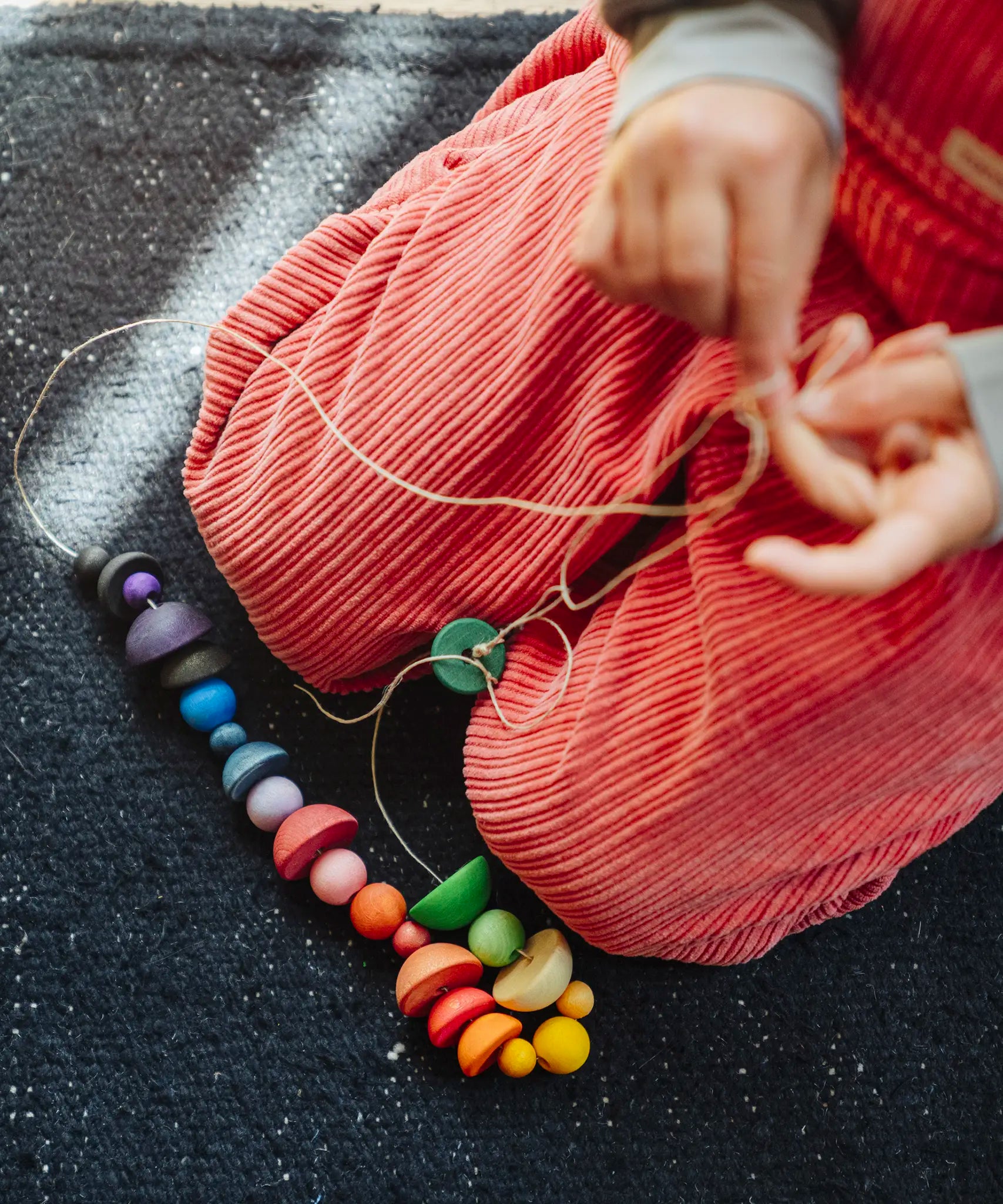 Close up of a child's hand threading colourful wooden beads onto a string from one of the gifts included in the Grapat 2026 advent calendar available at Babipur.