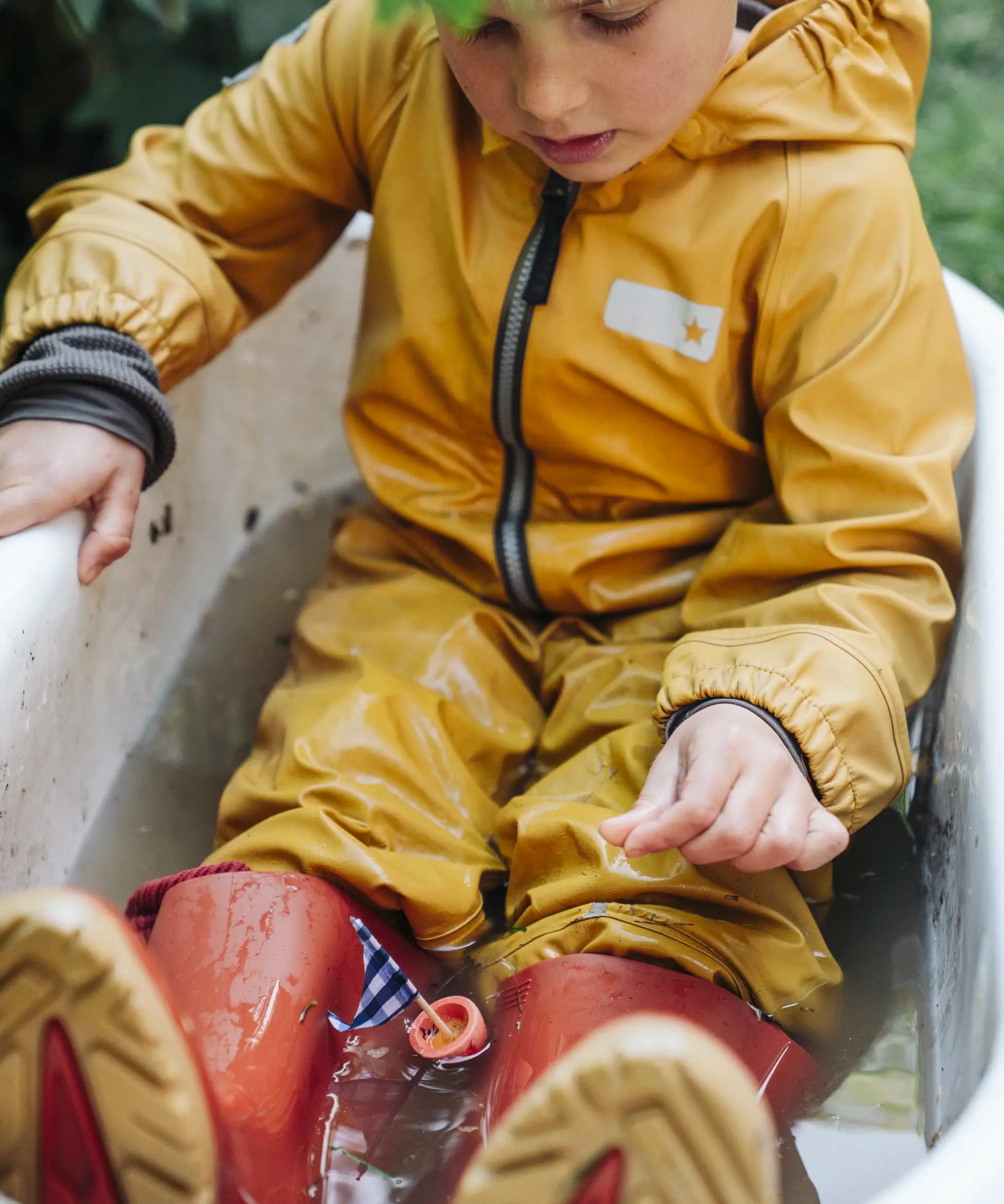 Child sitting in water playing with a small sail boat toy created using pieces from one of the gifts included in the Grapat 2026 advent calendar available at Babipur. 