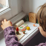 Child lining up small wooden toy pieces on the windowsill from the gift boxes included in the Grapat 2026 advent calendar available at Babipur. 
