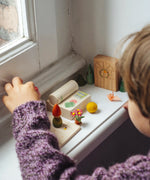 Child lining up small wooden toy pieces on the windowsill from the gift boxes included in the Grapat 2026 advent calendar available at Babipur. 