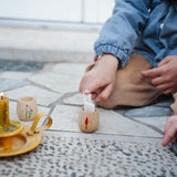 Child placing a piece of rolled up paper into a decorated wooden pot from one of the gifts included in the Grapat 2026 advent calendar available at Babipur. 