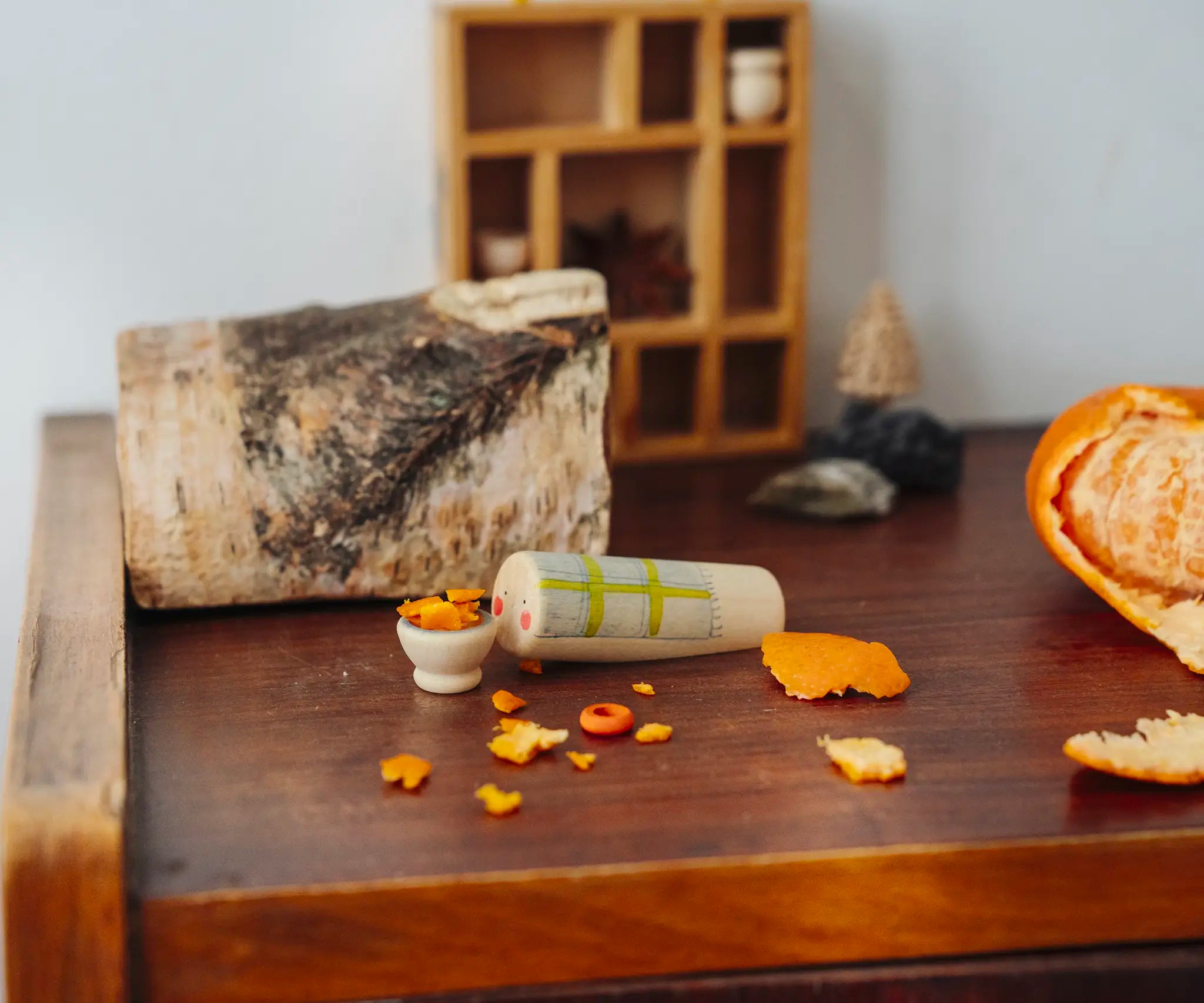 Wooden Tio log character with tangerine peel pieces placed ina  small wooden bowl. One of the gifts included in the Grapat 2026 advent calendar available at Babipur.