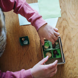 Overhead view of a child arranging wooden toy pieces in a box from one of the gifts included in the Grapat 2026 advent calendar available at Babipur. 