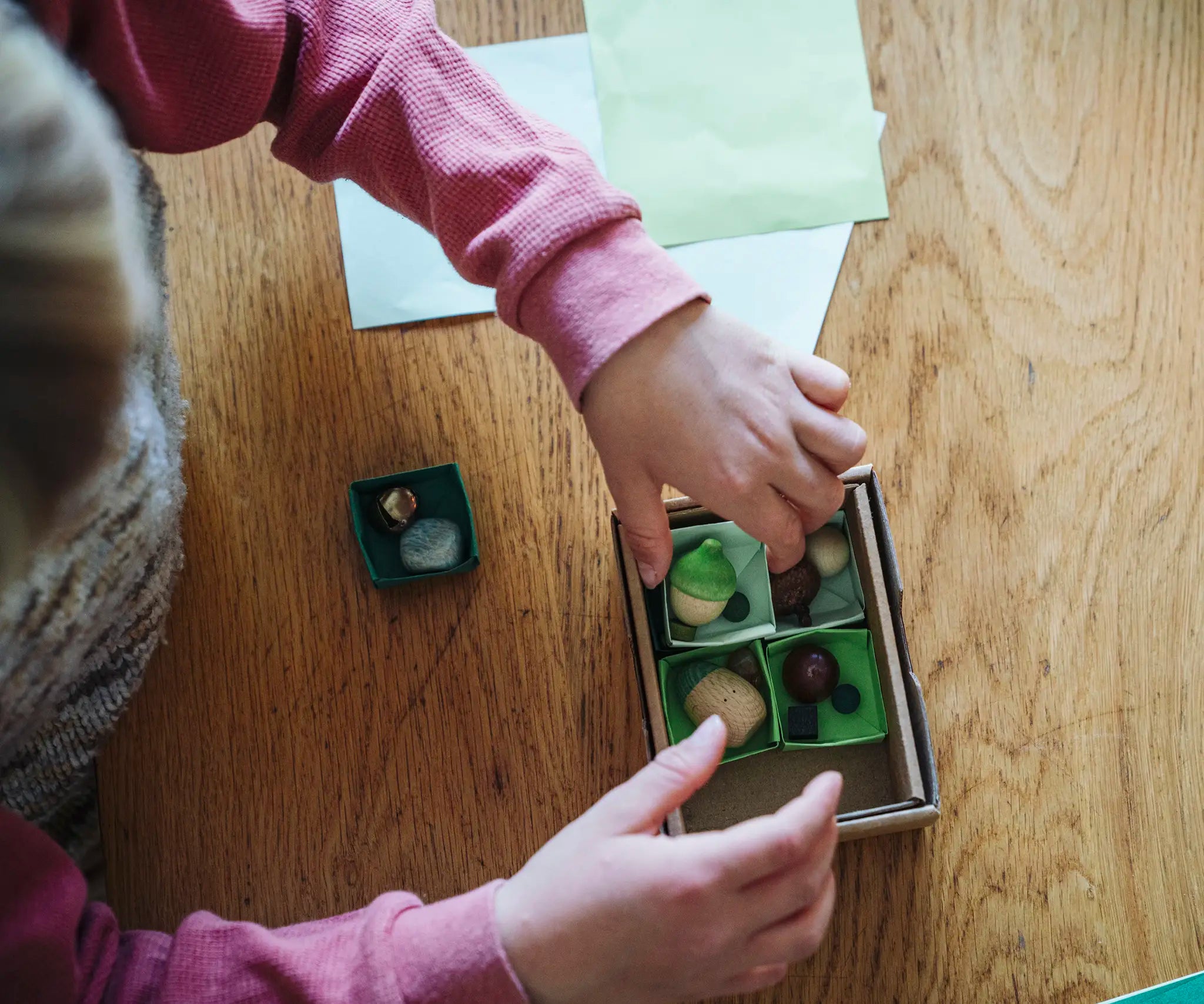 Overhead view of a child arranging wooden toy pieces in a box from one of the gifts included in the Grapat 2026 advent calendar available at Babipur. 