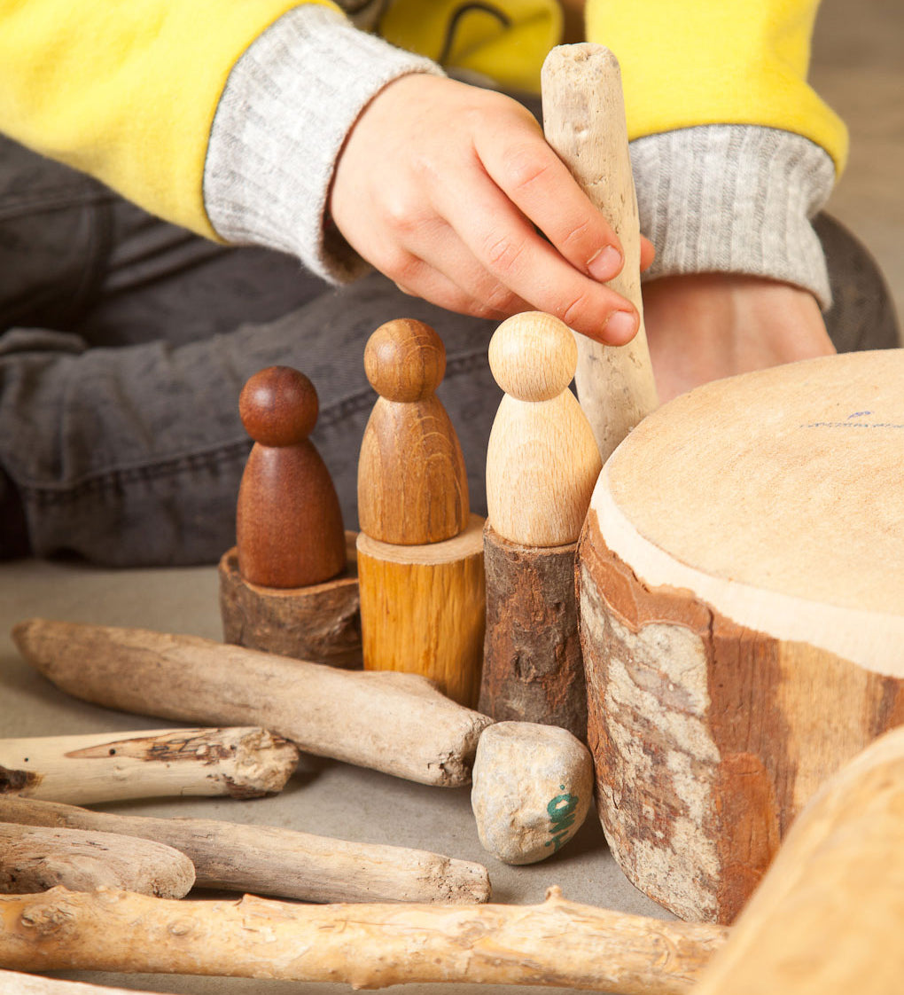 A close up of a child playing with the Grapat 3 Natural Nins. Three wooden peg dolls made from 3 different wood types. These wooden toys are part of a wide range of open ended toys available at Babipur.  