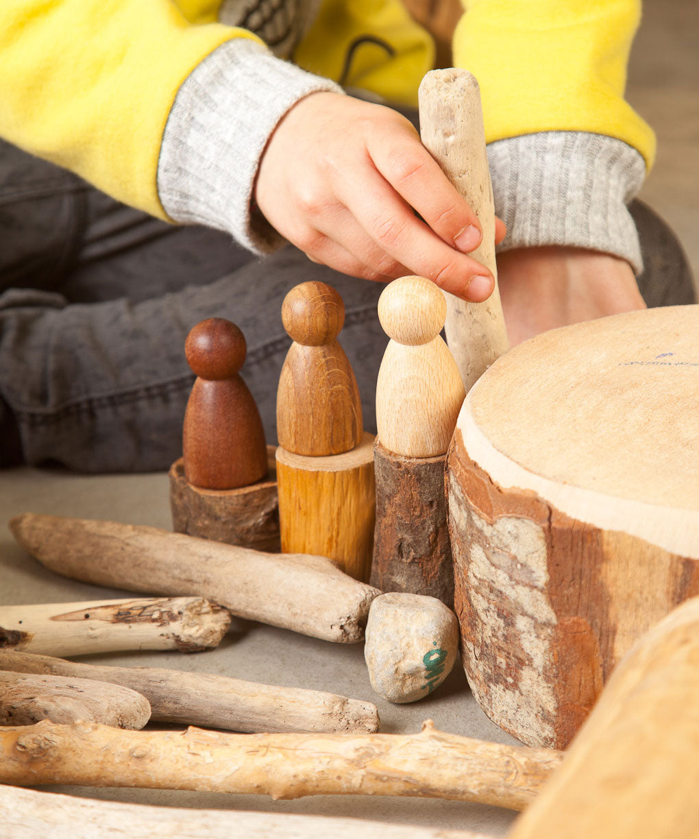 A close up of a child playing with the Grapat 3 Natural Nins. Three wooden peg dolls made from 3 different wood types. These wooden toys are part of a wide range of open ended toys available at Babipur.  