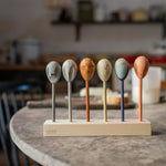 Grapat wooden twin soul puppets on a kitchen table resting on a wooden stand showing the different handcrafted faced puppets. Features a grey, brown, orange, blue handcrafted wooden puppet. 