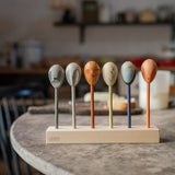 Grapat wooden twin soul puppets on a kitchen table resting on a wooden stand showing the different handcrafted faced puppets. Features a grey, brown, orange, blue handcrafted wooden puppet. 