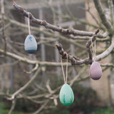 The Grapat Handmade Wooden Aurora Eggs Cold Colours Easter Decorations hung from tree branches outdoors.