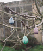 The Grapat Handmade Wooden Aurora Eggs Cold Colours Easter Decorations hung from tree branches outdoors.