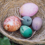 The Grapat Handmade Wooden Aurora Eggs Cold Colours Easter Decorations placed in a jute basket next to real dyed eggs. 
