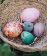 The Grapat Handmade Wooden Aurora Eggs Cold Colours Easter Decorations placed in a jute basket next to real dyed eggs. 