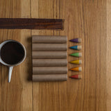 Birds eye view of 6 Grapat Baby Sticks lined up on a wooden coffee table next to a white mug of coffee.