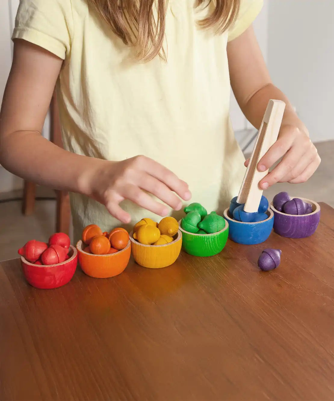 A child playing with the Grapat Wooden Toy Bowls and  Acorns Set. A set of 6 coloured bowls with wooden acorn shapes in matching pieces. 
