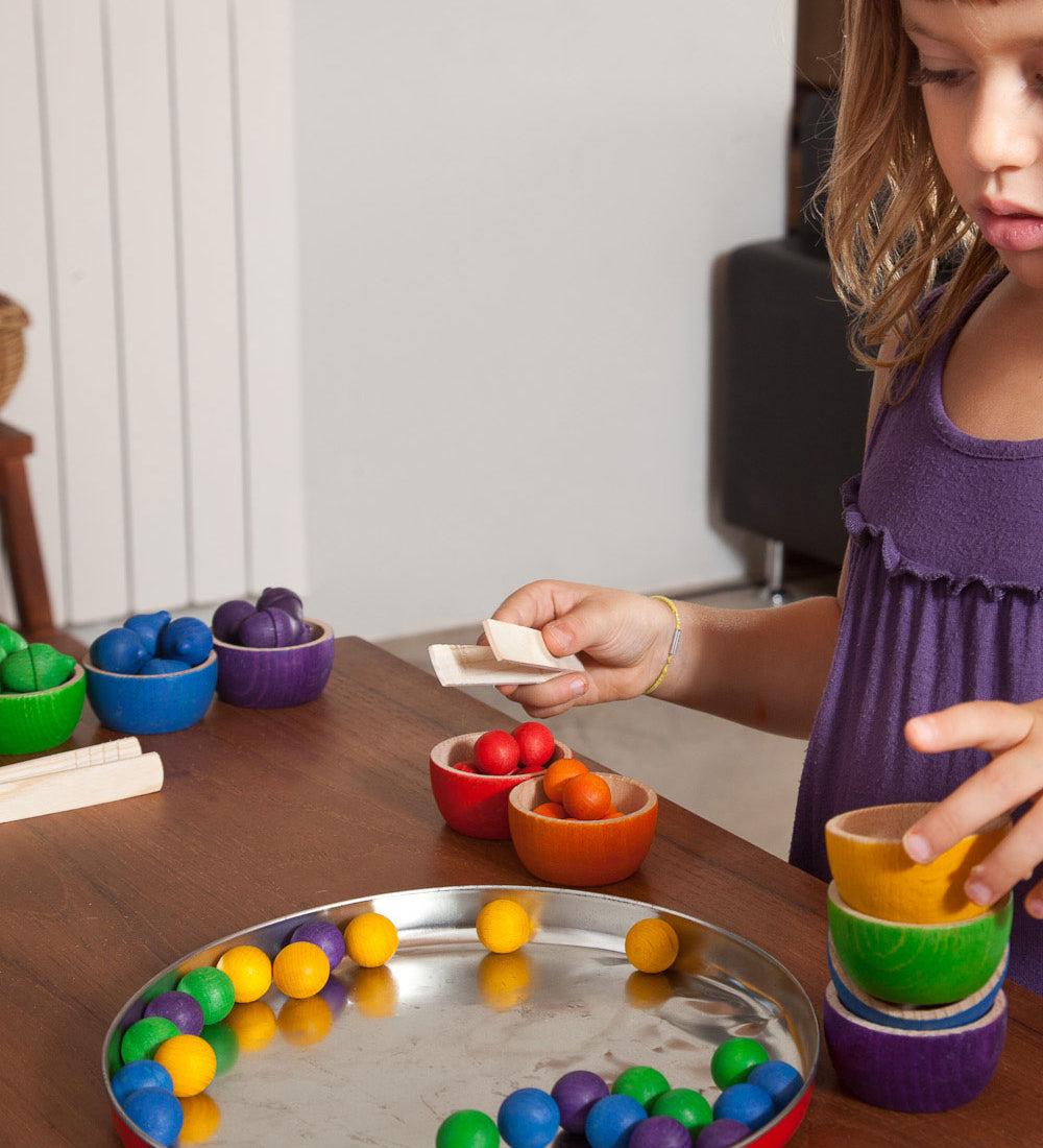 A child playing with the Grapat Wooden Toy Bowls and Marbles Set. A set of 6 coloured bowls with marbles in matching colours. These wooden toys are part of a wide range of open ended toys available at Babipur.  