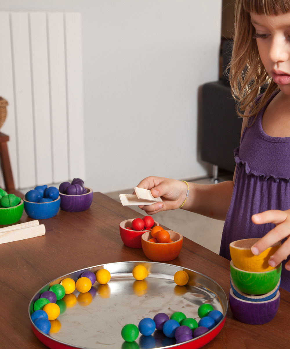 A child playing with the Grapat Wooden Toy Bowls and Marbles Set. A set of 6 coloured bowls with marbles in matching colours. These wooden toys are part of a wide range of open ended toys available at Babipur.  
