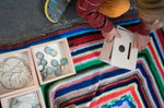 Close up of child crouched down next to some Grapat wooden boxes filled with bottle tops and paper shapes