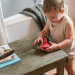 Child playing in the bathroom next to a wooden table with the Grapat wooden pink chill wobbly bird resting on top on the wooden table