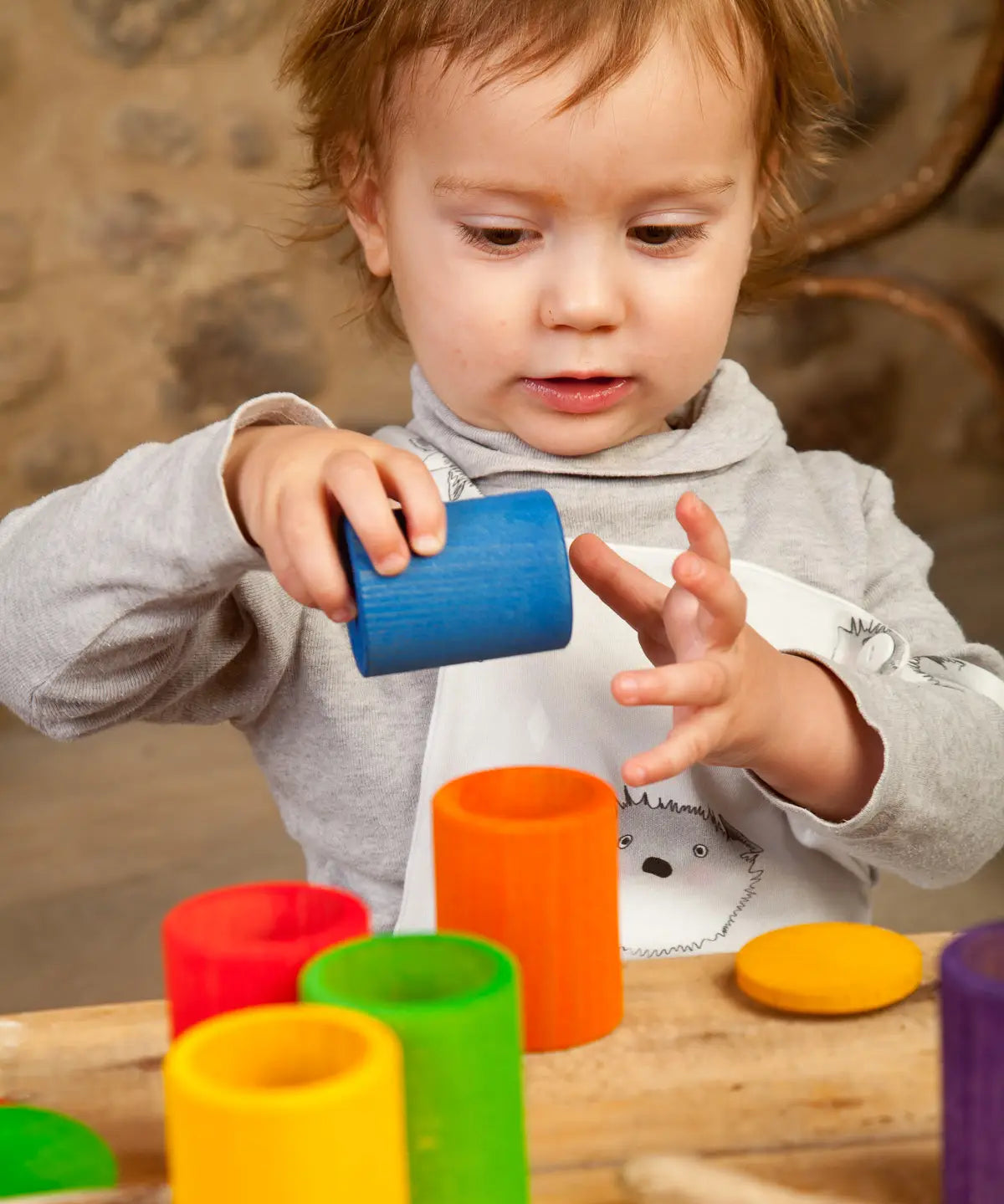Child holding a blue Grapat handcrafted wooden cup with lid next to other coloured cups on a table