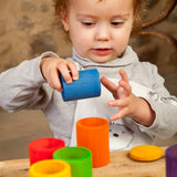 Child holding a blue Grapat handcrafted wooden cup with lid next to other coloured cups on a table