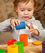 Child holding a blue Grapat handcrafted wooden cup with lid next to other coloured cups on a table