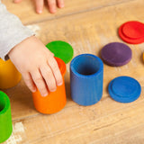 Child hand holding a orange Grapat handcrafted wooden cup with lid next to other coloured cups on a table