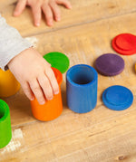Child hand holding a orange Grapat handcrafted wooden cup with lid next to other coloured cups on a table