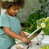 Close up of child playing with the eco-friendly Grapat baby nin toys on a white table next to a metal jug of flowers