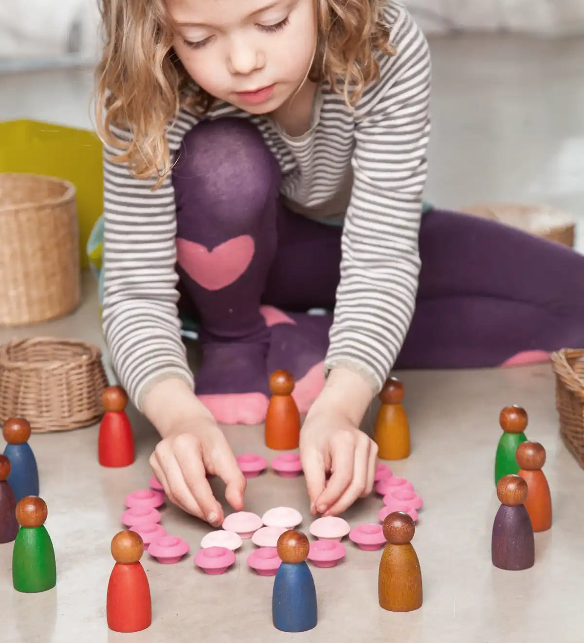 Child playing with cold and warm coloured dark wood Nins peg dolls. 