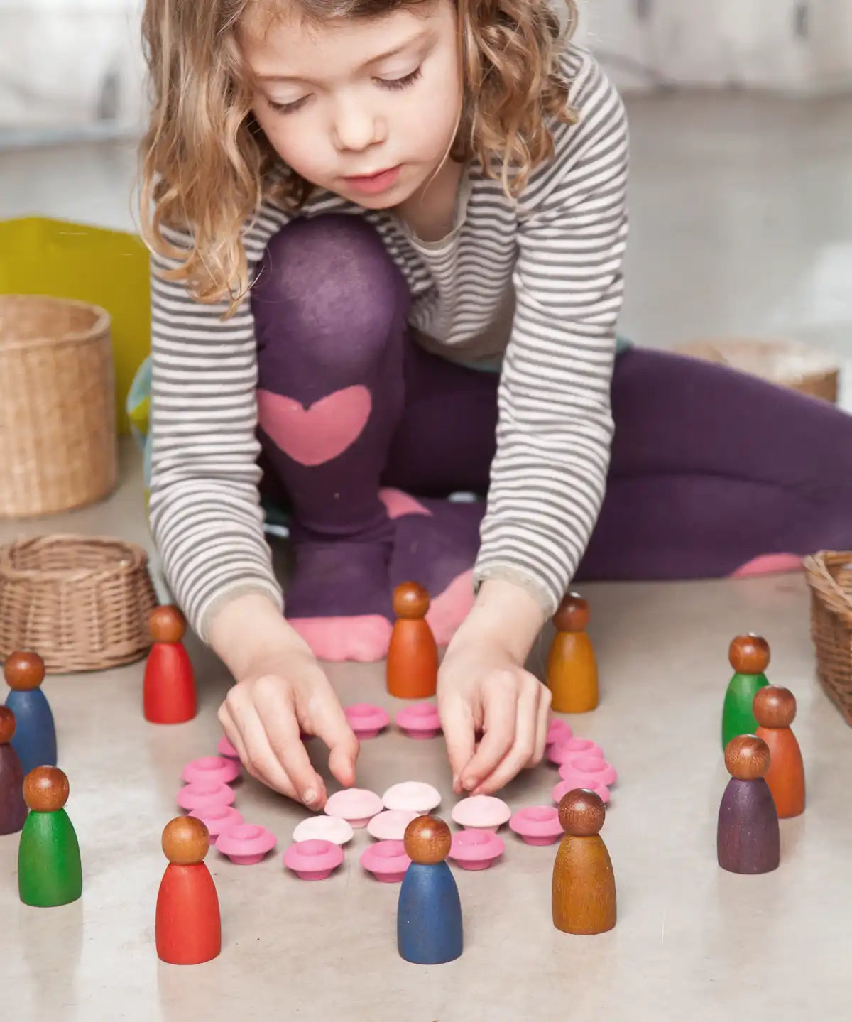 Child playing with cold and warm coloured dark wood Nins peg dolls. 