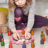 Child playing with cold and warm coloured dark wood Nins peg dolls. 
