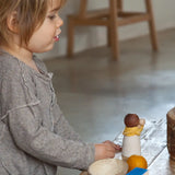 Child sitting next to a table with a standing Grapat waldorf adult nin peg doll