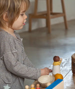 Child sitting next to a table with a standing Grapat waldorf adult nin peg doll