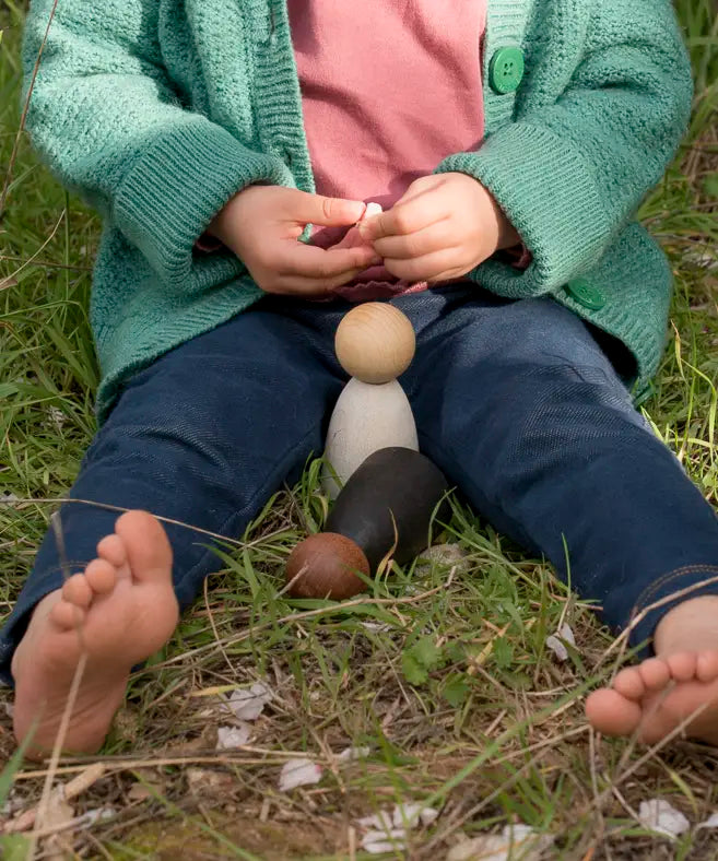 Child sitting on grass with Grapat waldorf adult wooden nin peg dolls  outdoors