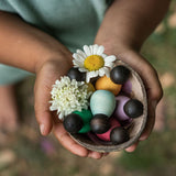 Grapat 6 Dark Baby Nins. A set of 6 small dark wooden baby Nin peg dolls in half a coconut shell, held in a child's hands. Grapat have a wide range of wooden toys and loose parts available at Babipur. 