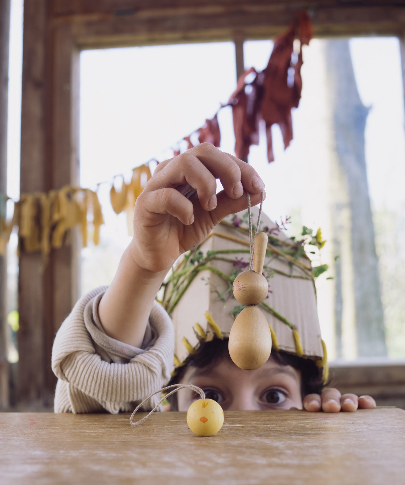 A child holding up the bunny from the Grapat handmade Wooden Easter Decorations Hop bunny and Peep chick set. The chick can be seen placed on a wooden table in front of them. 