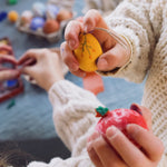 A close up of a child's hand holding the yellow coloured egg from the Grapat Handmade Sunrise Eggs Wooden Easter Decorations set.