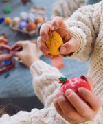 A close up of a child's hand holding the yellow coloured egg from the Grapat Handmade Sunrise Eggs Wooden Easter Decorations set.