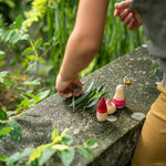 Close up of child playing with the Grapat yay wooden figures on a stone wall next to some green leaves