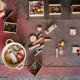 Child crouched on the floor surrounded by pieces of the Grapat handmade wooden Happy place toy set