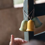 A close up of the light blue, yellow and green Grapat wooden jingle joy bells hanging on a chair